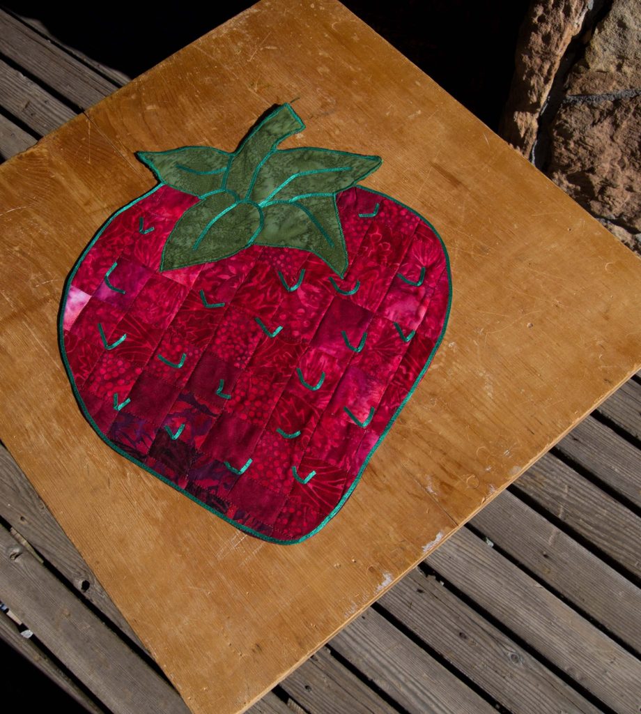 Bargello pattern table topper, rich red fabrics with a green leaf