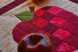 Closeup of a bargello apple appliqued on Sweet Harvest table runner - paperbacked fusible webbing used for sewing appliques on quilts